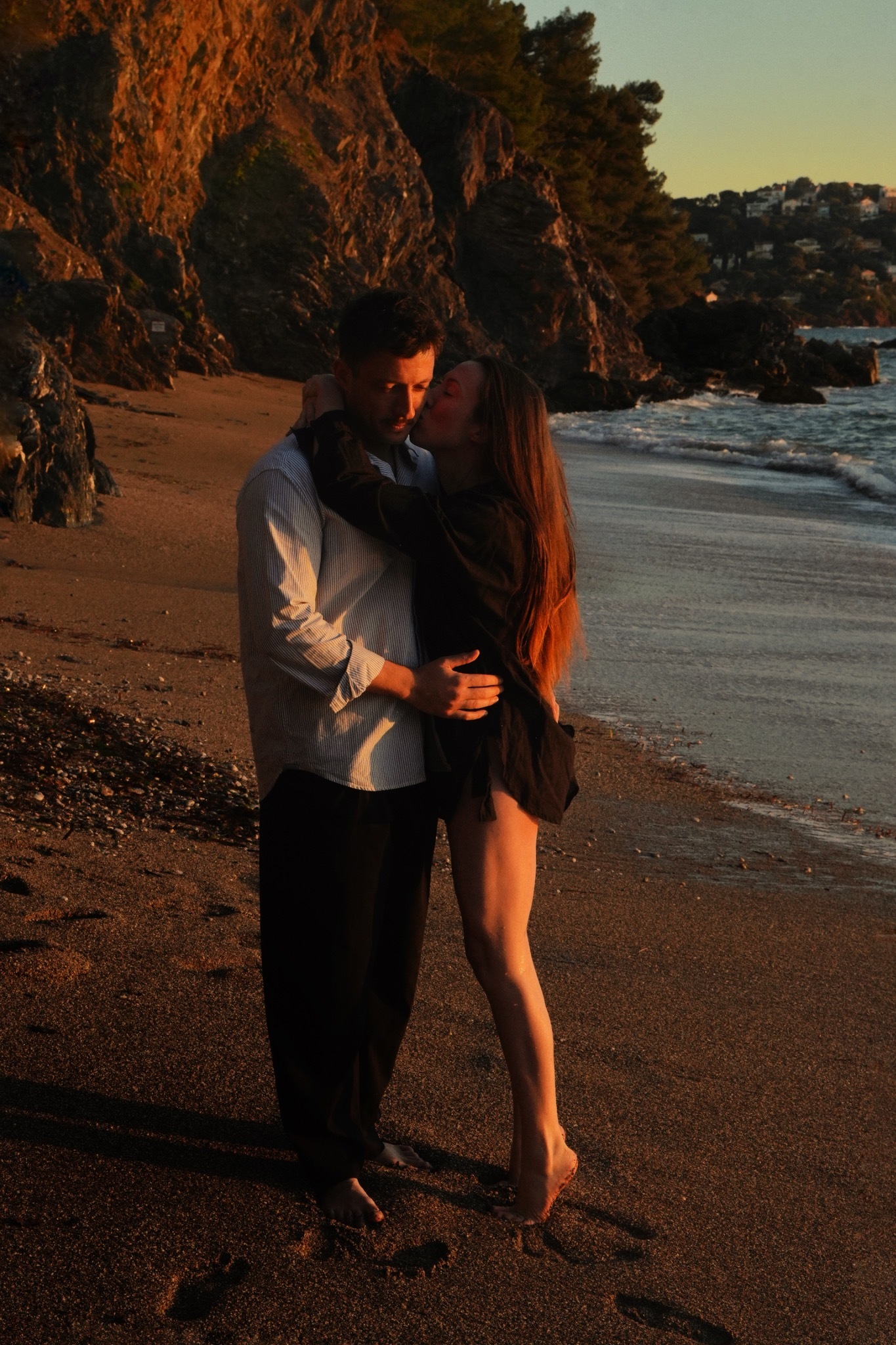 Un couple s’enlace sur la plage au pied des rochers