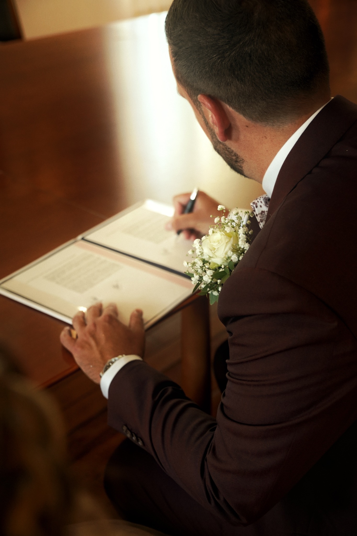 Le marié signe le registre, son bouquet posé près de lui