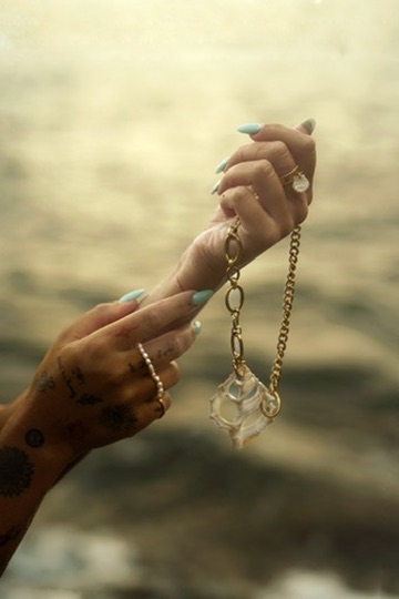 Des mains présentent un collier et son pendentif dans une lumière dorée